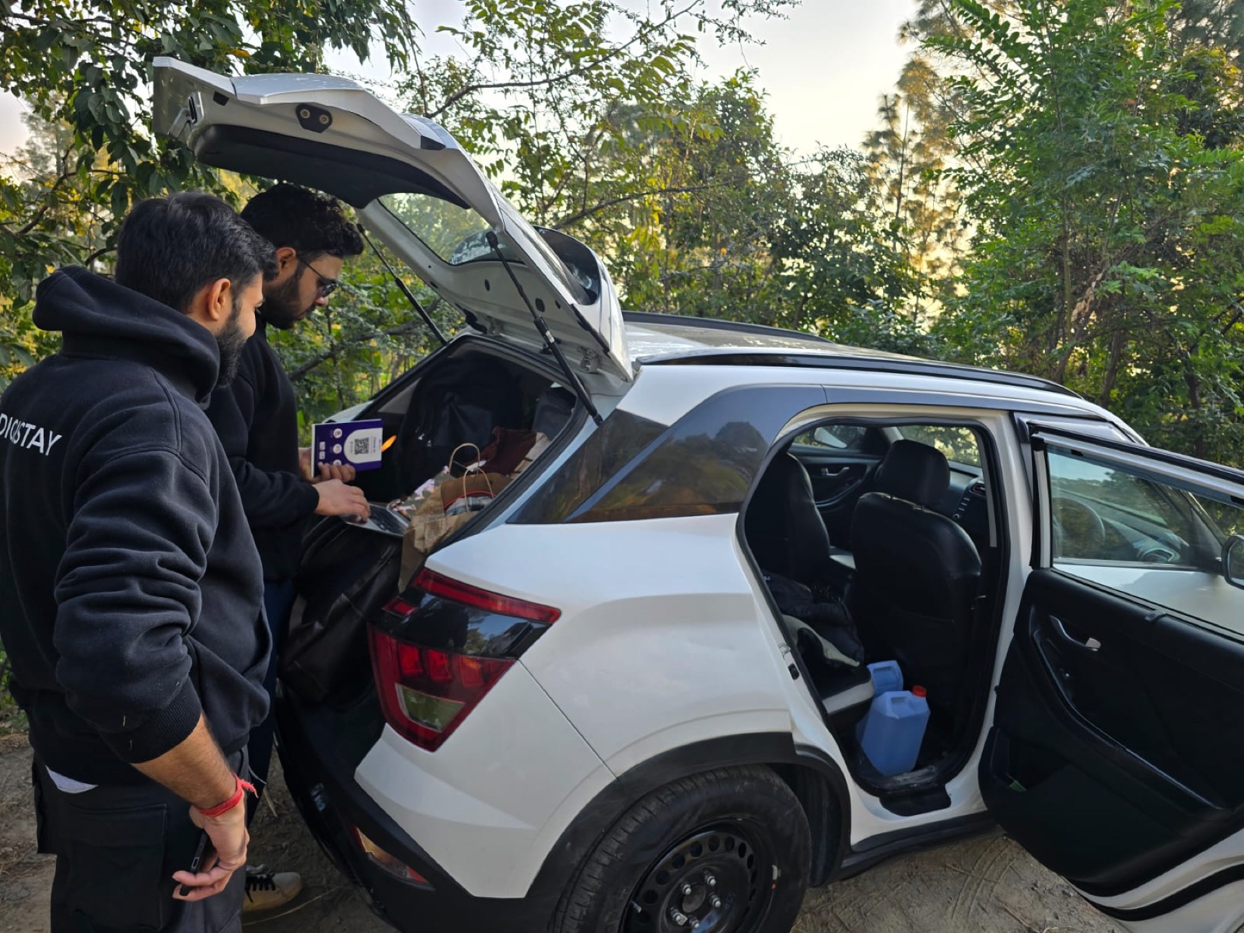 Two DigiStay teammates working on a laptop at a car boot during field onboarding.